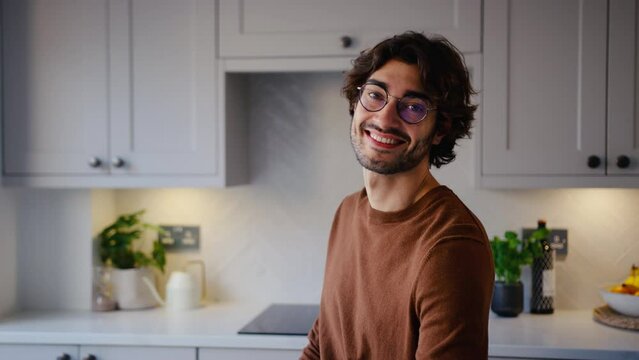 Portrait of smiling young man wearing glasses taking a break sitting at kitchen counter at home - shot in slow motion