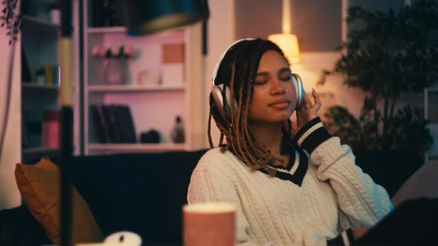 Pleased African American young woman listening to music in headphones, leisure