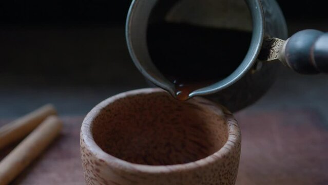 Pouring turkish coffee from Cezve into wooden cup. Close up.