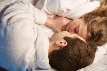 Top-view man and woman lying in bed face to face and hugging