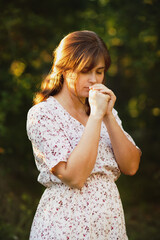 young woman praying on nature, girl thanks God with her hands folded under chin, concept of religion