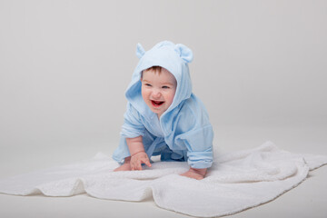 A cute happy laughing baby in a soft bathrobe crawls on a white background after bathing. The child...