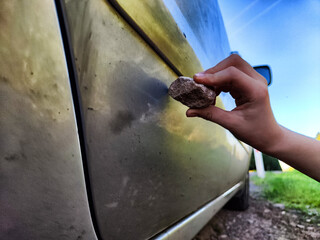 The child's hand with a stone scratches the side of the car. The concept of hooliganism, property damage, disobedient boy or girl - obrazy, fototapety, plakaty