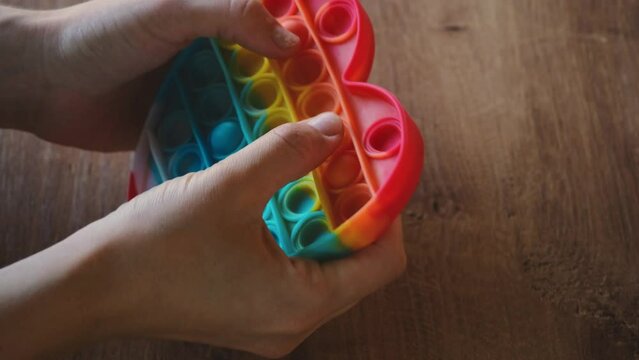Colorful rainbow antistress sensory toy fidget push pop it on human hand. Young woman plays simple dimple. Rubber multicolored heart in girl's hands, Trending things popular among children and adults.