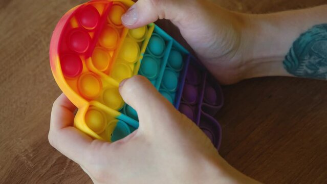 Colorful rainbow antistress sensory toy fidget push pop it on human hand. Young woman plays simple dimple. Rubber multicolored among as character. Trending things popular among children and adults