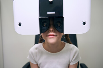 Young female patient sits in front of special apparatus for diagnosing vision