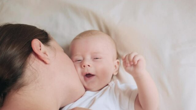 Close up top view happy loving mum with adorable smiling baby lying on cozy bed talk to cute infant with warmth kiss tender cheek. Affectionate mom caressing pampering little babe kid. Motherhood