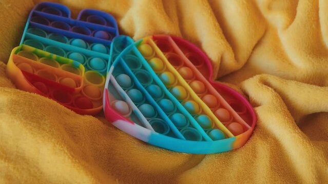 Rubber multicolored toys. Trending things popular among children and adults. Throw a toy pop it on a yellow plaid. Slow motion 4k horizontal footage. Top view. Heart and Character Among Us