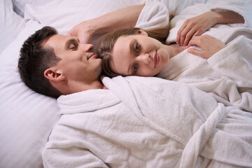 Happy woman and man in terry bathrobes lying in bed