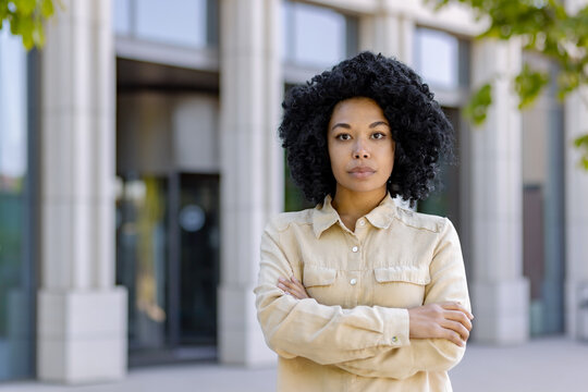 Portrait of confident serious business woman outside office building, aro american woman with crossed arms looking at camera.