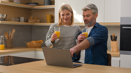 Moving shot Caucasian family adult middle-aged couple drinking healthy juice talking at kitchen buy...