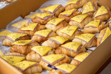 Appetizing croissant ham and cheese sandwiches in a paper box, enhanced with oregano spray.
