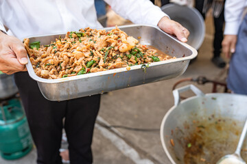 Experience the Thai Traditional flavors of Stir-Fried Basil with Pork, as it comes to life in a big pan cooked outdoors in a scenic field, with the expert touch of a turner.