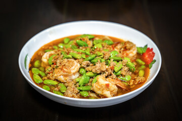 Fototapeta na wymiar Thai Stir-Fried Stink Beans with Shrimps and spicy shrimp paste sauce in white dish bowl on dark wood table. Clipping Path.