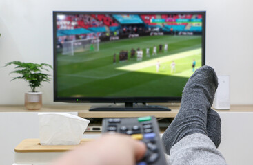 Watching football/soccer on TV, first-person perspective, holding remote control with feet up, nice and relaxed at home