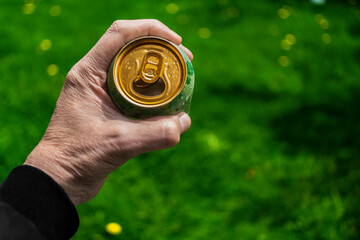 Male hand holding a can of beer with green blur background - relaxing and refreshing enjoyment in nature