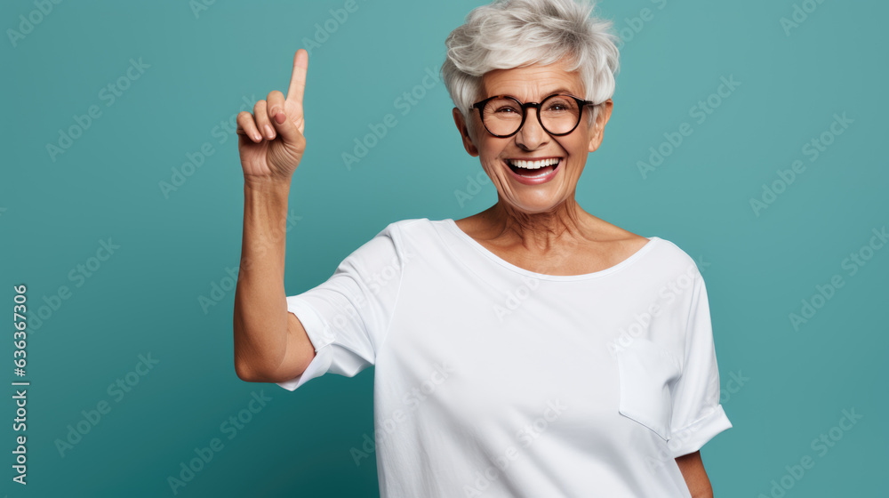 Wall mural Senior woman wearing white white T-shirt pointing with hand and finger to the side looking at the camera.