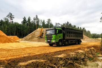 Fototapeta premium a crawler excavator loads sand into a truck. Large hills and heaps of sand, gravel, crushed stone of yellow, gray and black colors