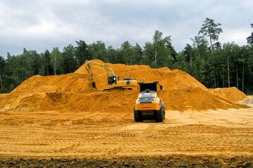 a crawler excavator loads sand into a truck. Large hills and heaps of sand, gravel, crushed stone of yellow, gray and black colors