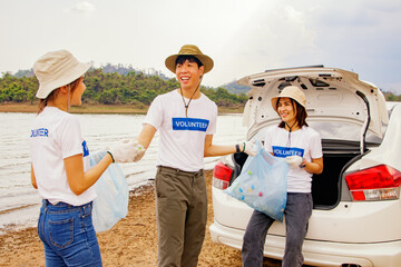 Asian volunteer teamwork unites as a teamwork collecting plastic bottles in bags and cleaning natural attractions by helping to carry garbage into cars for recycling to preserve the environment.