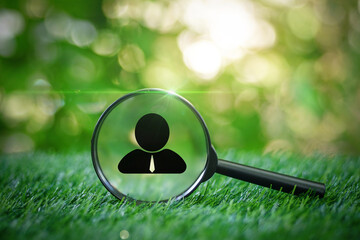Magnifying glass focused on a person symbol on the grass in garden with green nature environmental...
