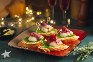 Mini sandwiches with pear, smoked duck and arugula in the shape of a Santa Claus hat on a square plate on a green concrete background. Merry Christmas concept. - obrazy, fototapety, plakaty