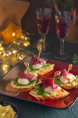 Mini sandwiches with pear, smoked duck and arugula in the shape of a Santa Claus hat on a square plate on a green concrete background. Merry Christmas concept.