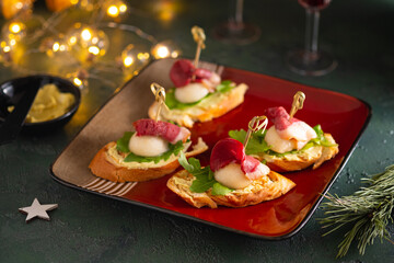 Mini sandwiches with pear, smoked duck and arugula in the shape of a Santa Claus hat on a square plate on a green concrete background. Merry Christmas concept.