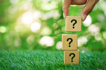 Hand placed a wooden block with question mark sign on stacking of them, laying on a natural background.Concept of quiz, many question arising.Environmental idea, front view, copy space.
