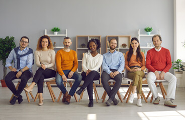 Happy smiling male and female audience sitting on row of chairs in modern cozy office room. Diverse group of positive young and old people enjoying interesting business event or club meeting