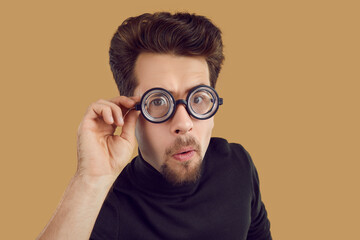 Portrait of funny alert and curious man looking at you through glasses with enlarged lenses. Close...