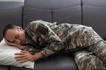 blurred boy looking at exhausted dad in camouflage sleeping on couch in living room with christmas decoration