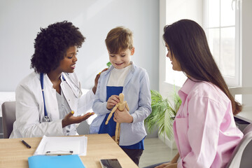 Caring female pediatrician talking to small boy patient and his mother in hospital. African American doctor, general practitioner examining little patient in medical office. Children healthcare