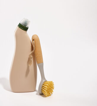 A beige detergent bottle and a eco friendly wooden brush with a long handle for cleaning and scrubbing. Copy space for text.