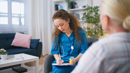 The female doctor prescribes medication to a senior patient, as part of the home care services - obrazy, fototapety, plakaty