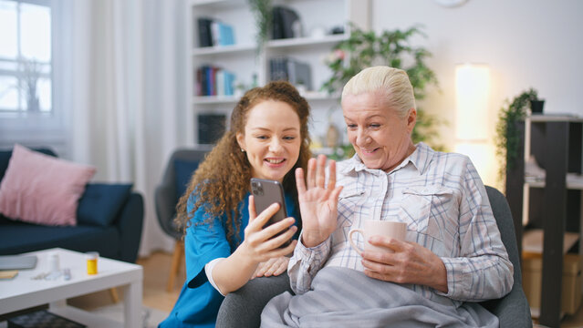 Elderly woman is having conversation with her relatives online, using a smartphone provided by a social worker