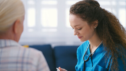 Nurse with a stethoscope filling out medical forms, listening to female patient - obrazy, fototapety, plakaty