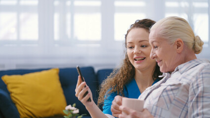 Retirement home worker helping mature woman to make a video call on smartphone