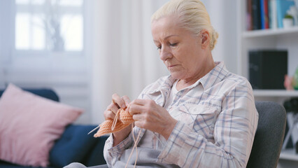 Sad senior woman knitting, sitting at home alone, retirement hobby, loneliness