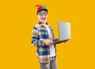 Portrait of funny nerd boy holding laptop computer. Laughing teenage boy wearing thick glasses, cap...