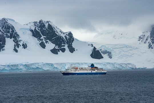 Large sailboat  pictured in front of a stunning backdrop of snowy mountainous terrain in Antarctica
