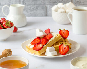 A plate with waffles smeared with cream cheese with strawberries and marshmallows, a bowl with...