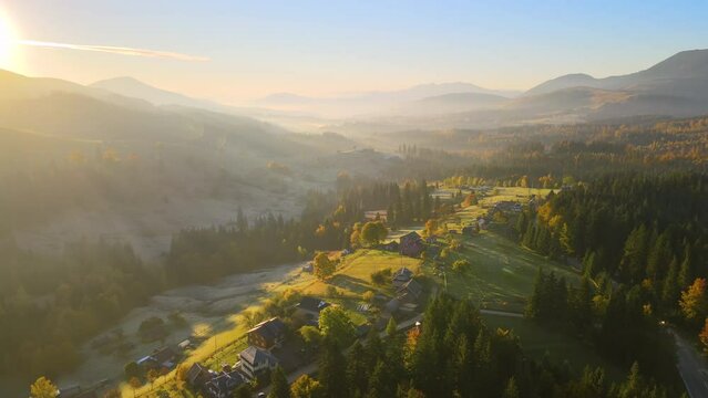 Wooded hills of Carpathian mountains in Ukraine with small traditional village houses at sunset. Brightly illuminated with setting sun evergreen woods with scattered local homes at fall season
