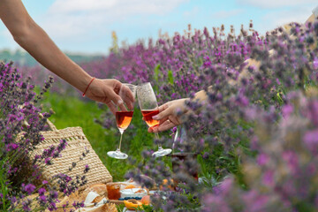Wicker basket with delicious food for a romantic picnic in a lavender field, wine, fruits, berries.