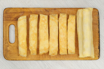 Homemade semi-finished products on wooden board. Frozen pancakes with filling twisted into rolls. Preparations of homemade food.