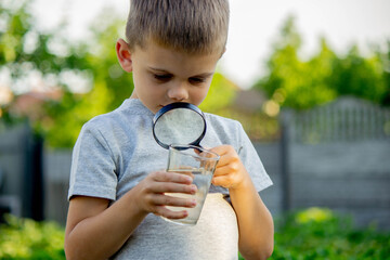 The child boy looking at water in a glass through magnifying glass. Selective focus.