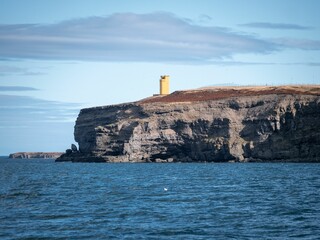a lighthouse sits on the cliff overlooking the ocean and a rocky cliff formation - Powered by Adobe