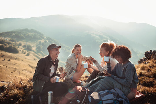 Young diverse group of female friends having a coffee break after hiking in the hills and mountains
