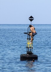 Obraz premium Teenage boys scaling a tall white buoy in the sparkling blue waters of Marsalforn, Gozo, Malta