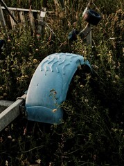 Vertical shot of an old abandoned and broken blue fender in the garden